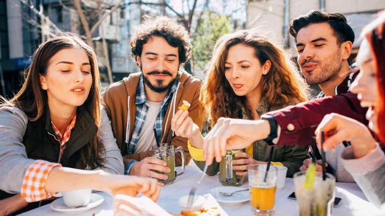Grupo de millennials comparte comida y bebidas al aire libre, representando distintos tipos de consumidores.