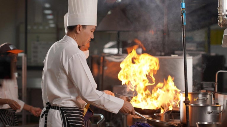 Chef cocinando con sartén en llamas en una cocina profesional, en plena acción culinaria 