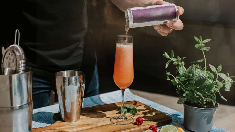 Persona sirviendo una bebida artesanal en copa alargada, decorada con menta, cítricos y frutos rojos