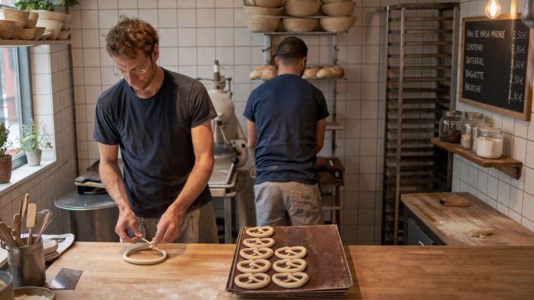 Panaderos elaborando masa en cocina compacta con bandejas listas para hornear en espacio reducido