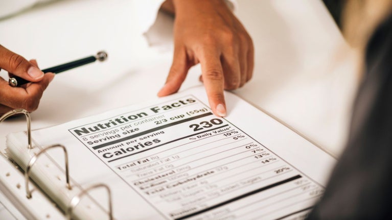 Persona señalando etiqueta nutricional en documento con información de calorías y composición.