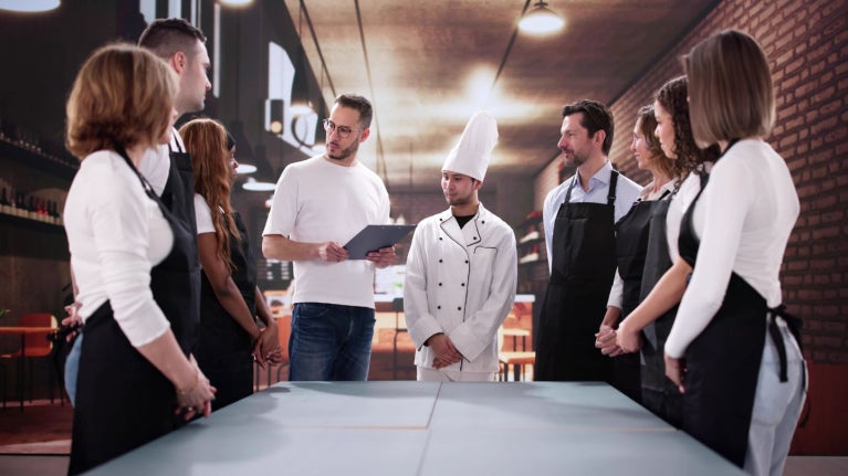 Grupo de personas reunidas en cocina profesional mientras una persona explica con una tablet