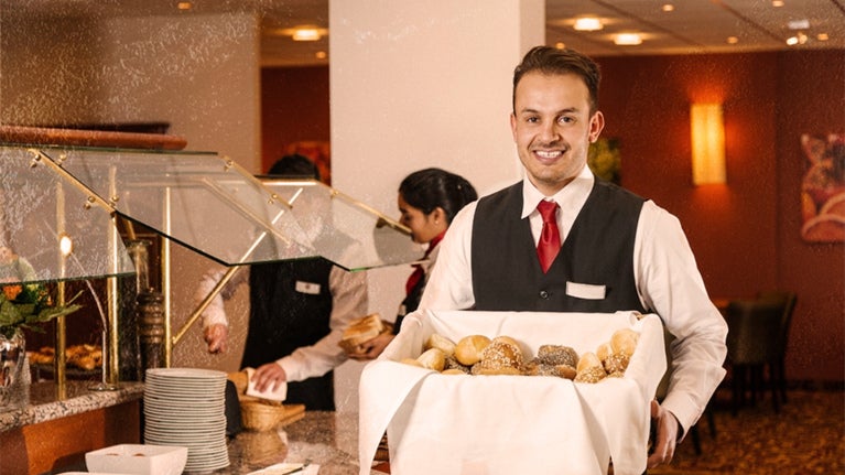 Mesero sostiene una caja con panes para surtir el buffet de un hotel