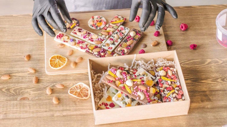 Repostera coloca barras de chocolate artesanal decoradas con frutos secos liofilizados en una caja.