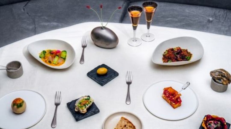Varios platillos gourmet servidos sobre una mesa con mantel blanco y dos copas de vino fino. 