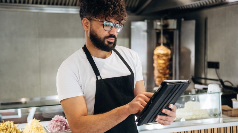 El propietario de un restaurante registra pedidos en una tableta digital junto al mostrador.