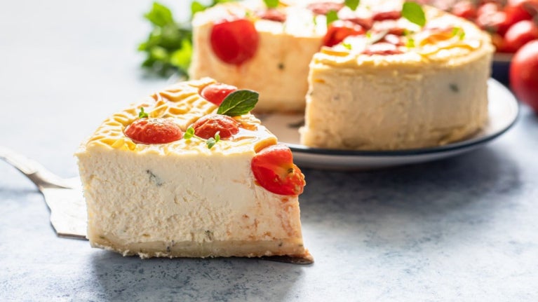 Rebanada de pastel salado de queso decorada con tomates cherry sobre una espátula de servir.