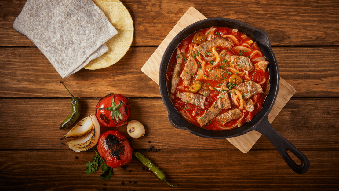 Estofado en sartén de hierro fundido junto a verduras rostizadas y tortillas de maíz