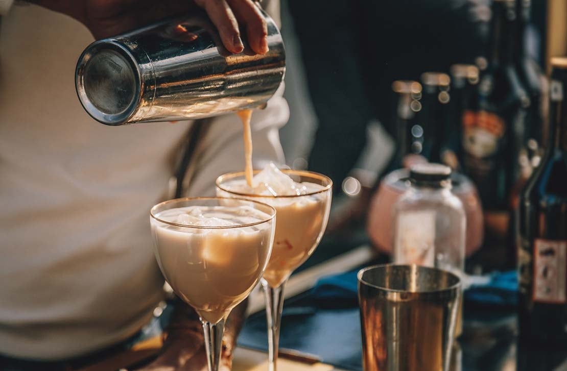 Sobre una mesa con botellas, un barista prepara dos cocteles de café para la cena de fin de año