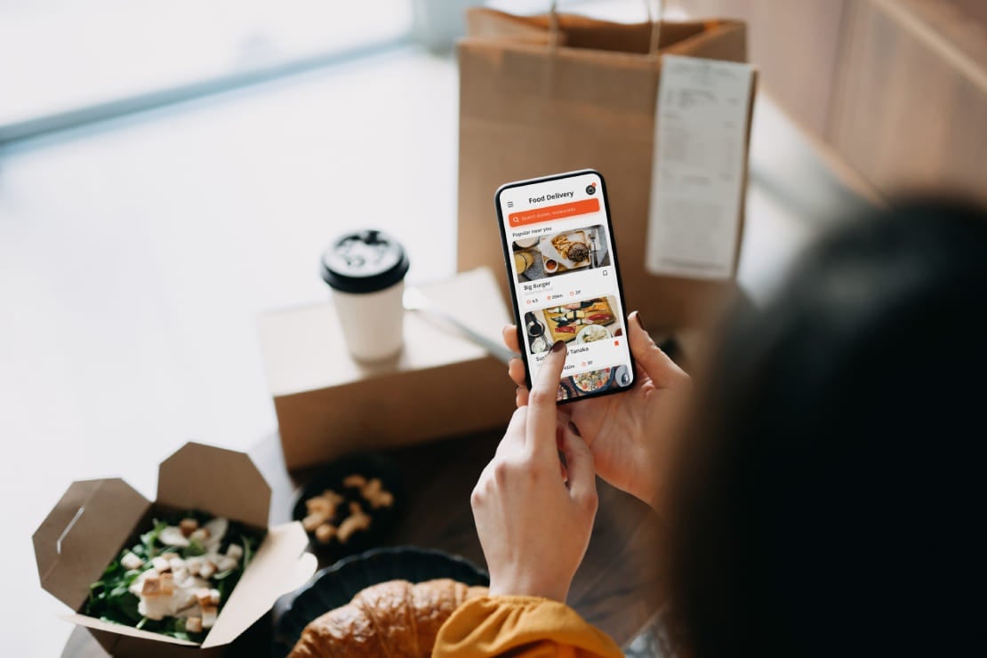Mujer con dos cajas de comida y una bebida al frente revisa en su app de delivery que su entrega a domicilio sea correcta