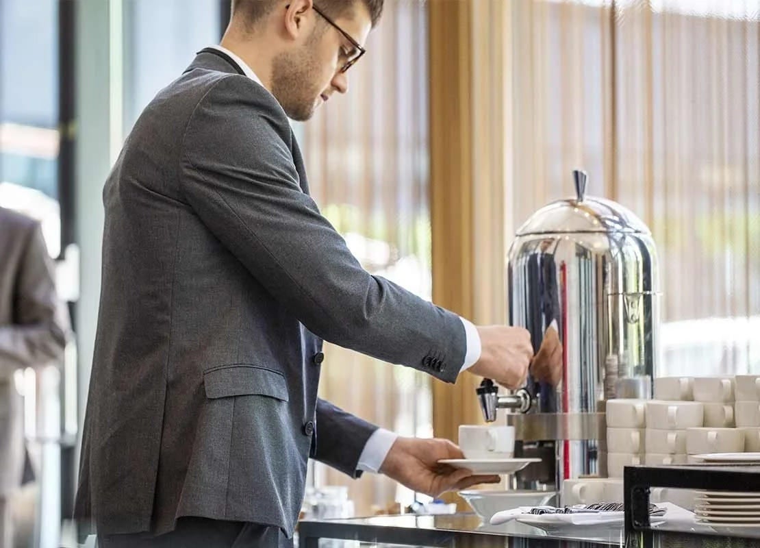 Participante de un evento corporativo sirve un café NESCAFÉ® de una cafetera dispuesta por un servicio de catering