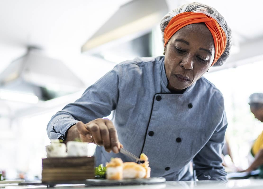 En una cocina de restaurante, una chef decora cuidadosamente un platillo que será fotografiado con técnicas de food styling