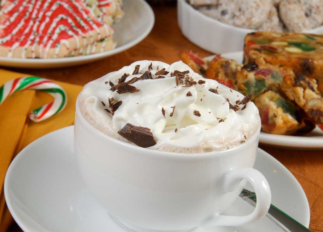 Una taza de cappuccino caliente con nata montada, tarta de frutas y postres navideños que hacen un buen maridaje