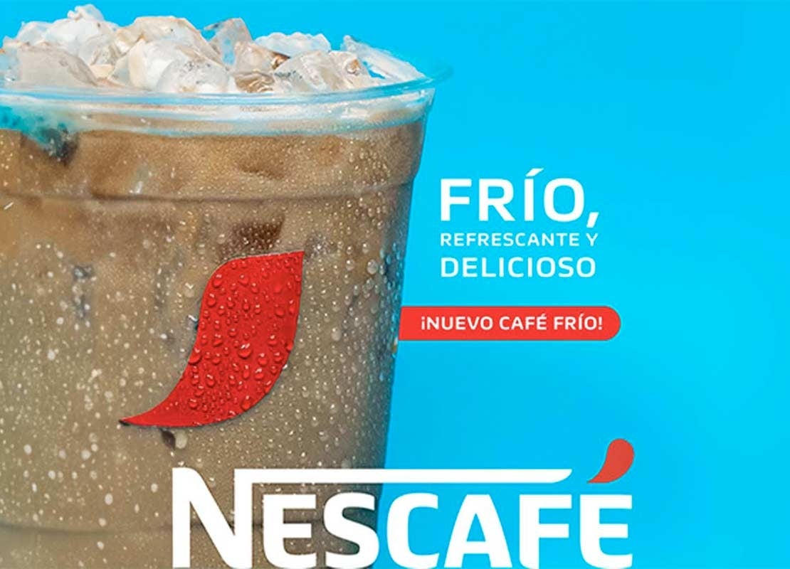 Sobre un fondo azul cielo, un vaso de café frío NESCAFÉ® en el que flotan cubos de hielo
