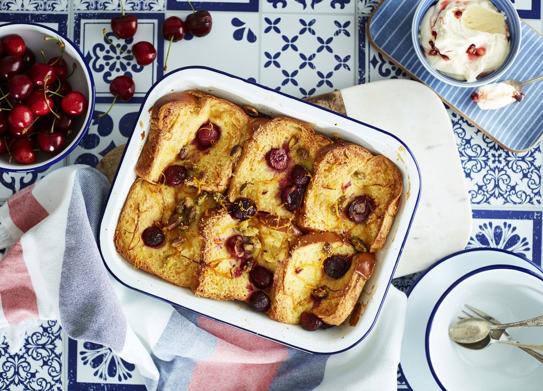 Bandeja de aluminio con 6 torrijas decoradas con fruta y mantequilla y alrededor una taza con cerezas y otra con helado