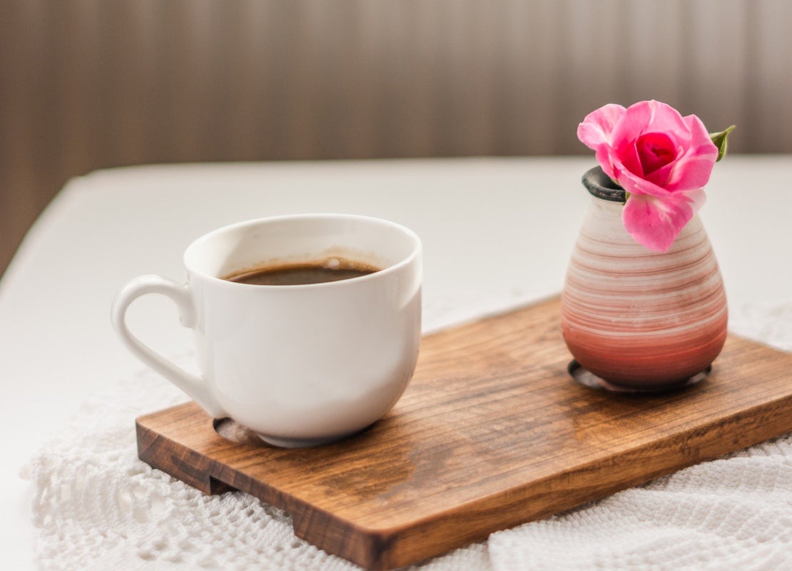 Sobre una tabla, una taza de café y una rosa en un jarrón como souvenir para obsequiar en el Día Internacional de la Mujer