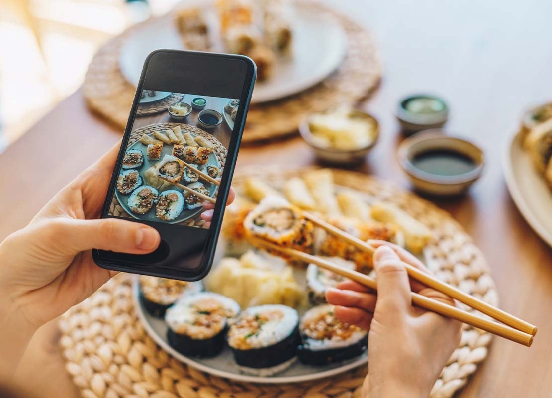 Influencer toma foto con su celular a un plato con diferentes rollos de sushi servidos en la mesa en un servicio de catering