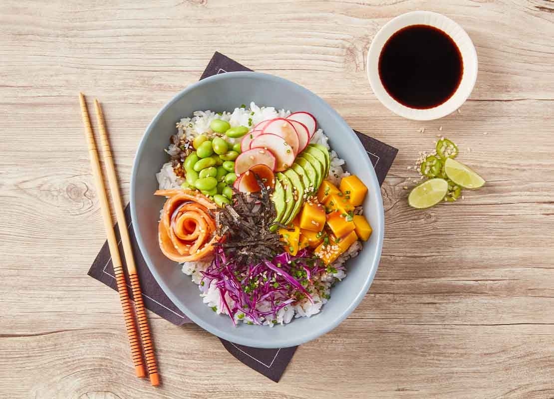 Poke bowl compuesto de arroz, vegetales y pescado acompañado de salsa de soya, una receta umami