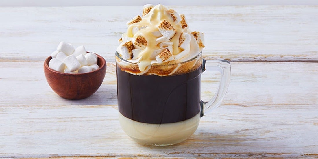 Taza blanca de café bombón decorado con crema batida, leche condensada y masmelos
