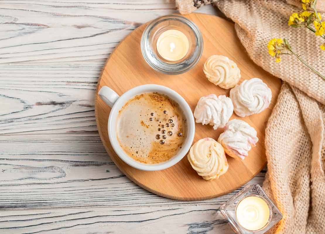 Sobre una tabla, una taza de café americano acompañado de profiteroles y decorado con velas y flores
