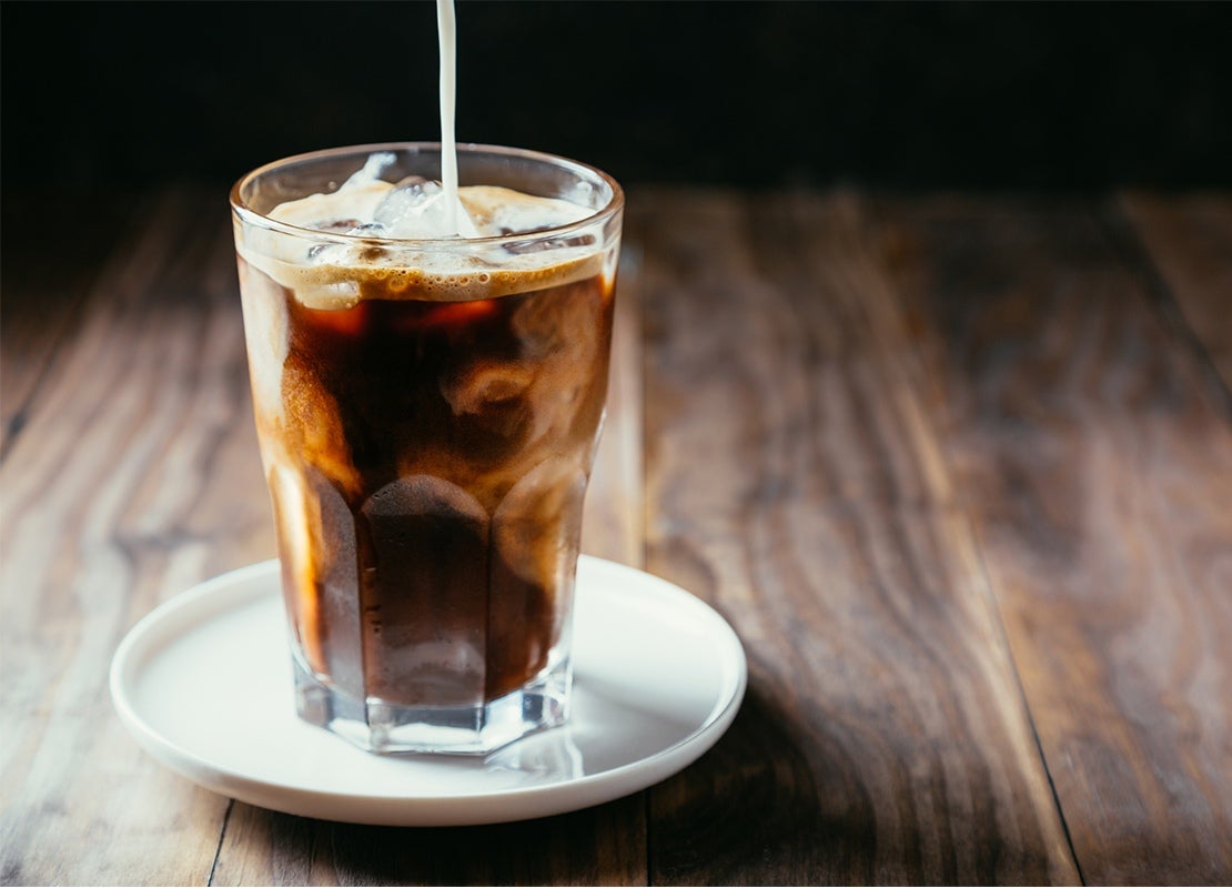 Café frío preparado con NESCAFÉ®, cubos de hielo y una bebida vegetal la cual se está vertiendo