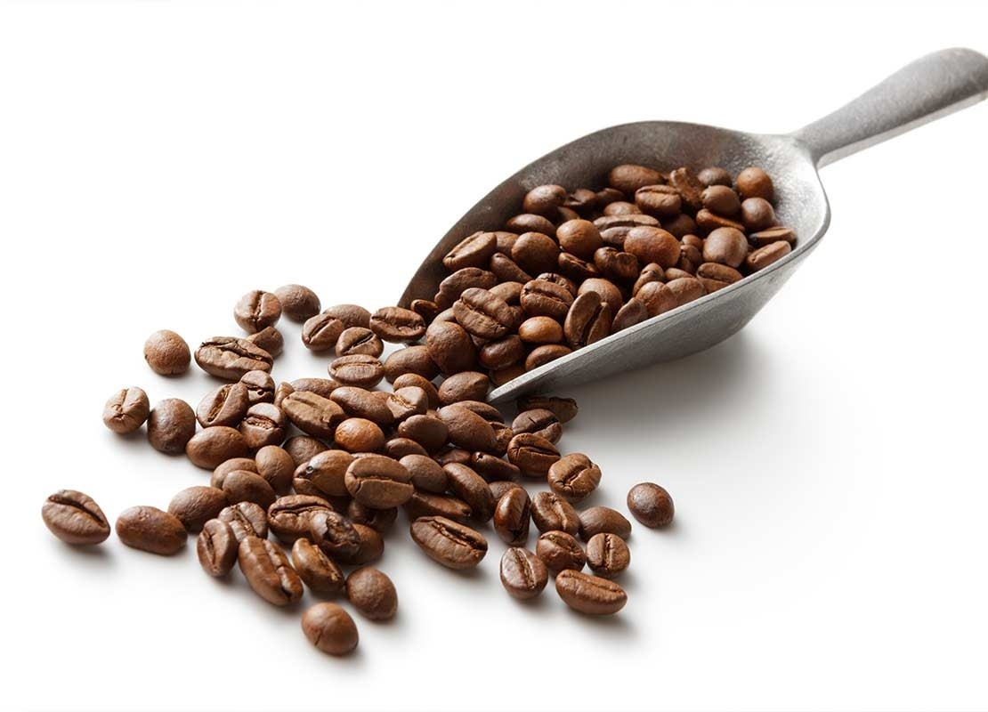 Granos de café tostado dentro y frente a una pala de acero inoxidable