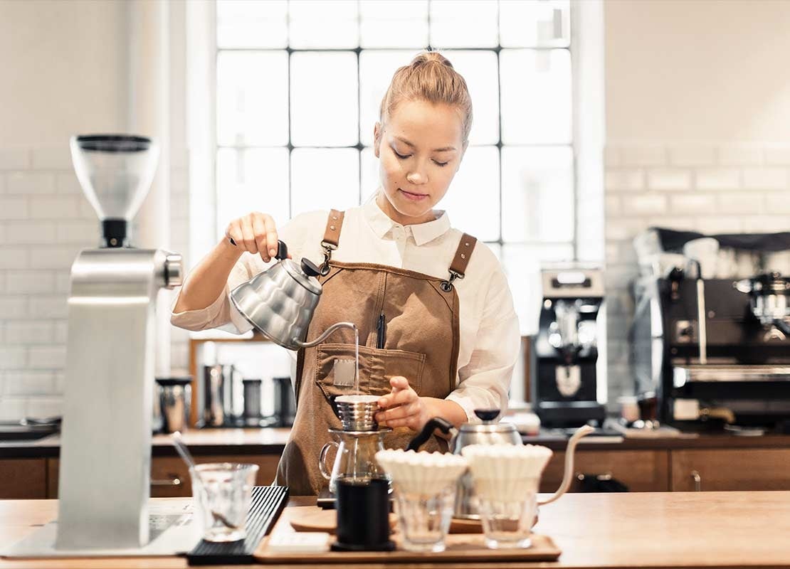 Barista prepara café al verter agua caliente con una tetera sobre un filtro de un dripper en una cafetería