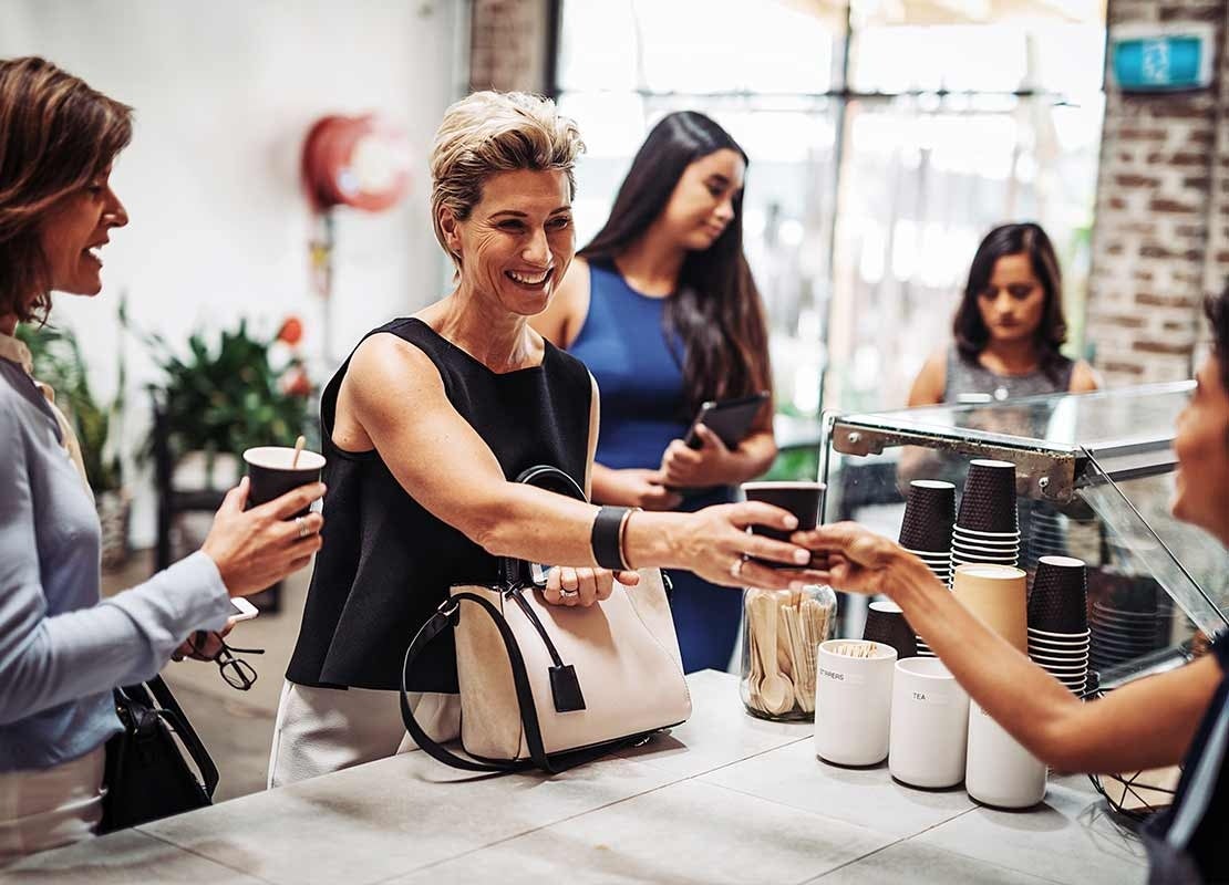 Clienta recibe una bebida de una trabajadora frente al mostrador de una cafetería con vasos