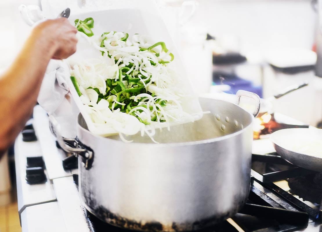 Mano de chef vierte vegetales en una olla puesta sobre la estufa para elaborar fondos de cocina