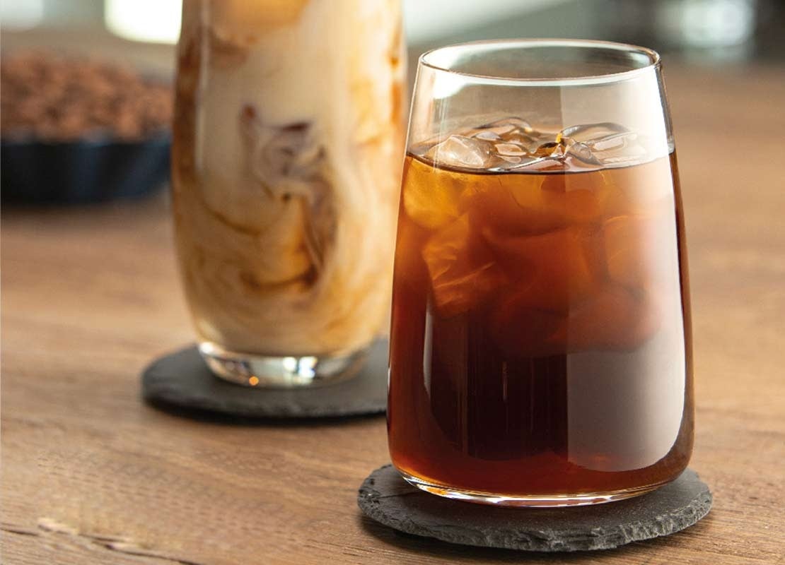 Dos vasos de café frío con hielo de diferentes tamaños y formas sobre portavasos negros