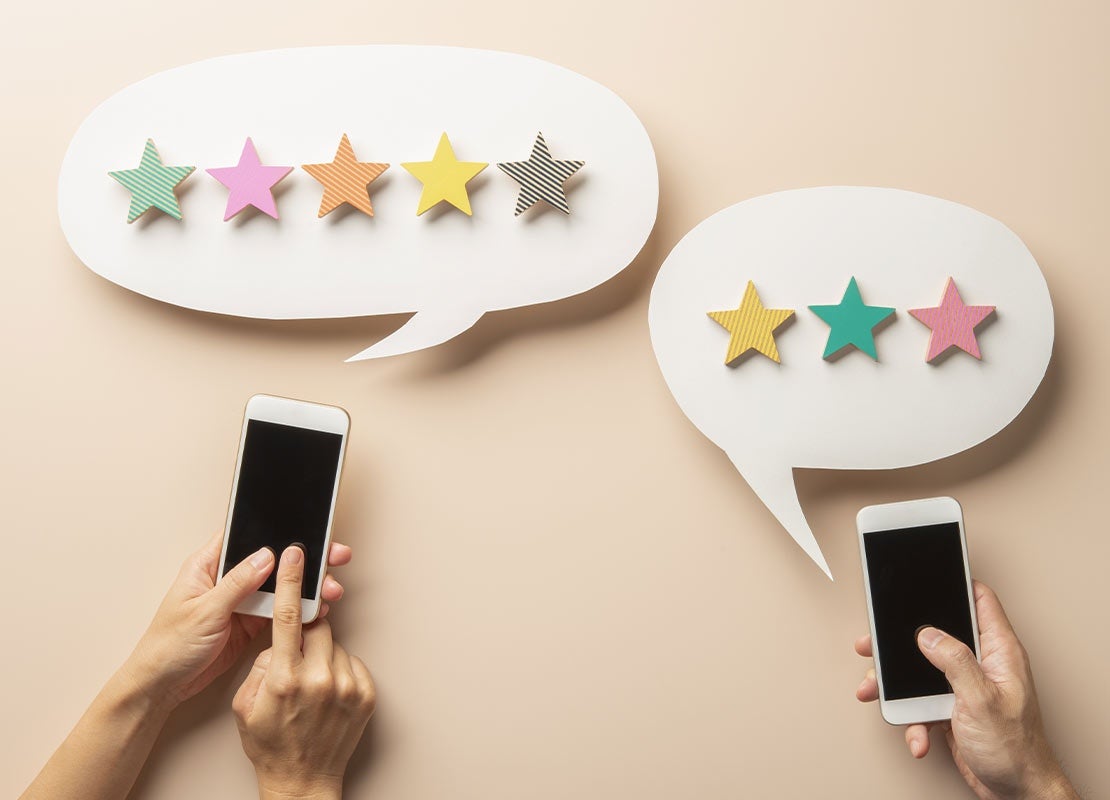 Manos tocan la pantalla de 2 celulares con burbujas de diálogo que contienen estrellas de calificación
