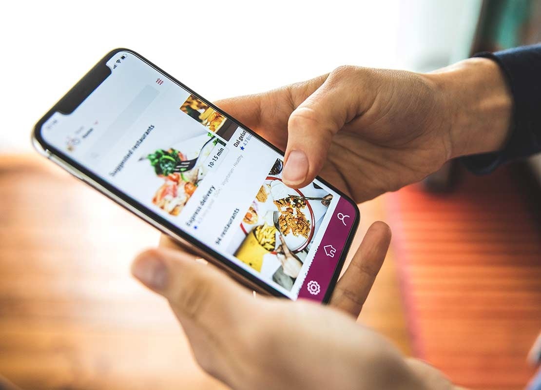 Persona sostiene un celular en el que revisa platos en la app de domicilios de un restaurante