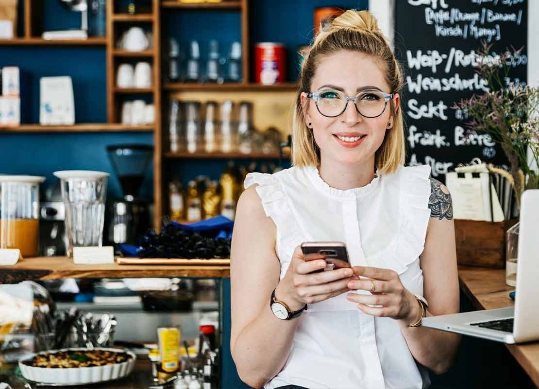 Dueña de un restaurante con un celular y un computador revisa su sistema POS en la nube