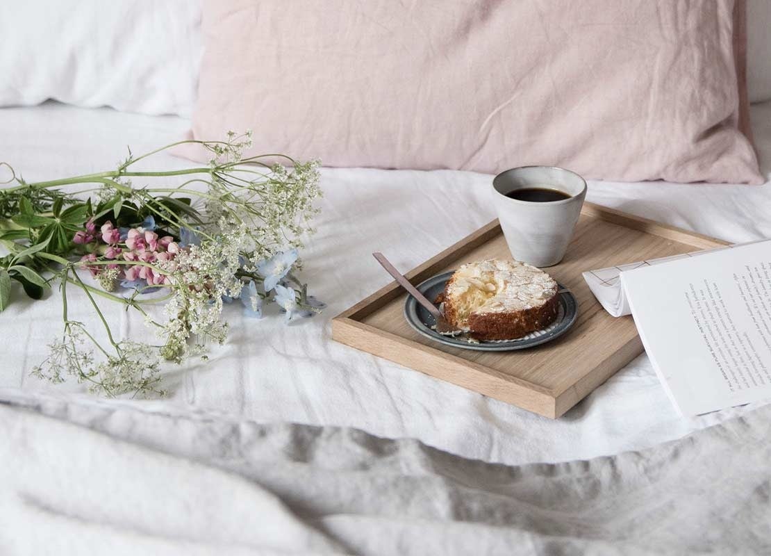 Bandeja con café y postre sobre una cama de la habitación de un hotel que tiene flores