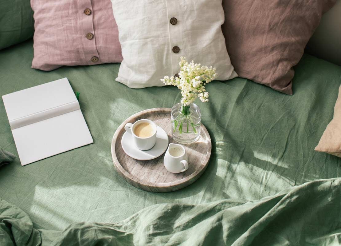 Cama de la habitación de un hotel con almohadas de colores y un servicio de café y leche sobre una bandeja