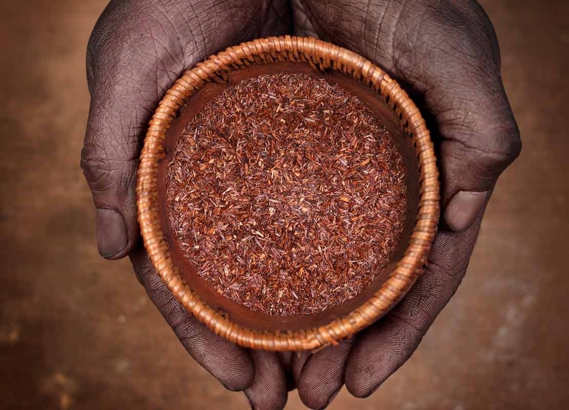 Manos juntas sostienen un vaso con diseño tradicional con una bebida de Rooibos infusionado