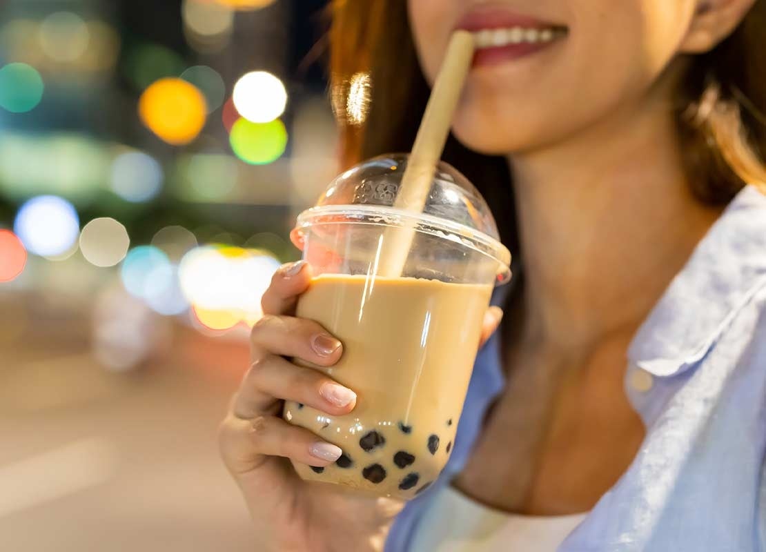 Mujer bebe un bubble tea en un vaso plástico con pitillo y con perlas al fondo que sostiene en su mano