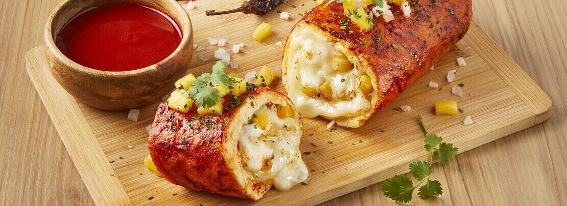 Sobre una tabla de cortar, rollo de pollo al pastor y taza de salsa elaborados con productos culinarios 