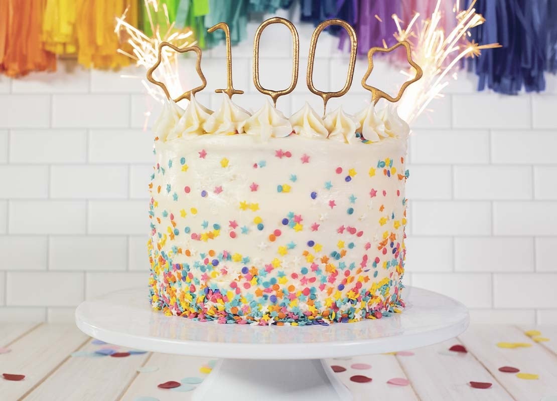 Pastel decorado con sprinklesm, velas tipo bengala y topper con el número 100
