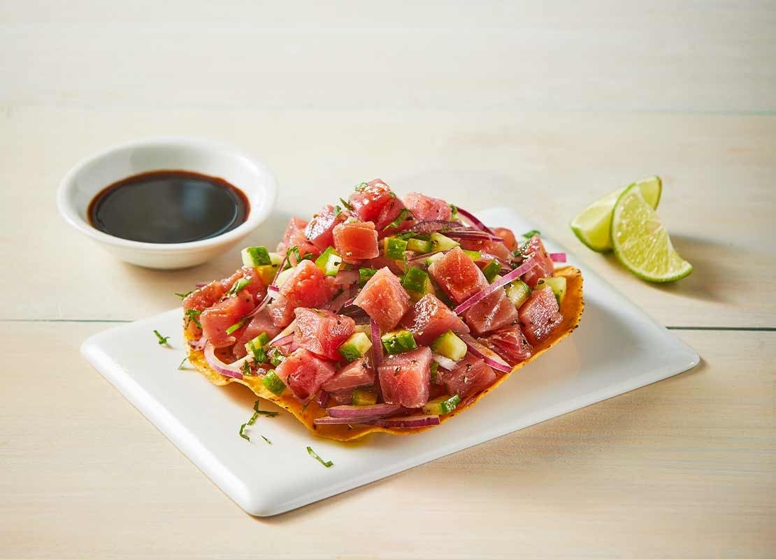 Plato con ceviche sobre una “lámina” de plátano, al lado rebanadas de limón y salsa de soya