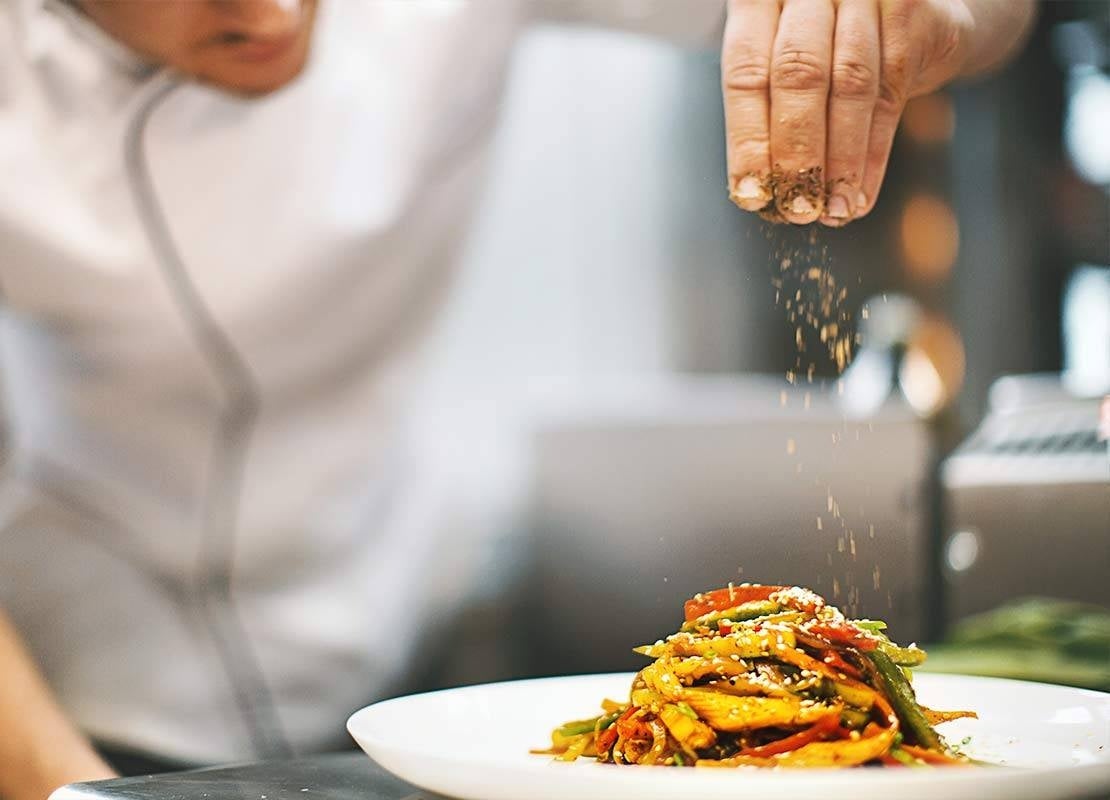 En una cocina de un cliente, chef finaliza un plato agregando una pizca de especias