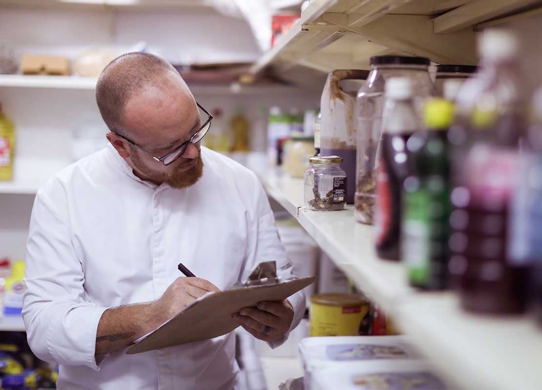 Chef revisa el inventario de un almacén de un negocio de food service y realiza anotaciones en su planilla
