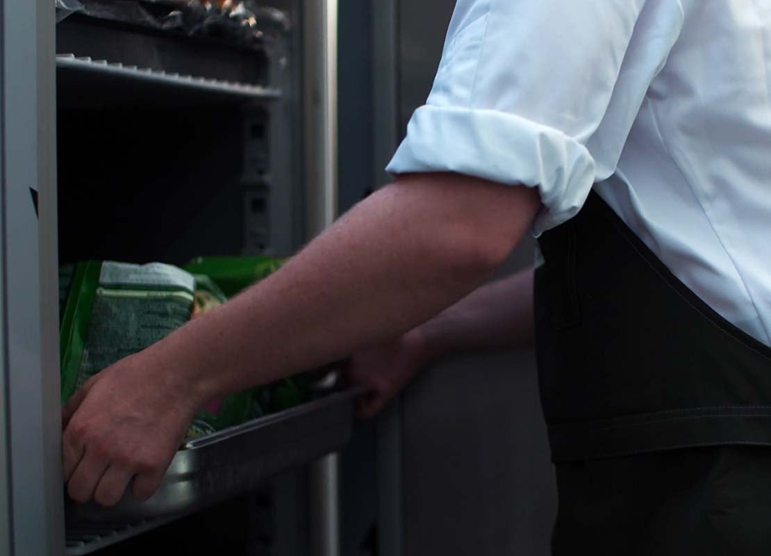 Ayudante de cocina retira una bandeja con alimentos refrigerados de un congelador industrial