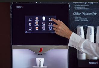 Una máquina NESCAFÉ® dispensa una bebida mientras un usuario selecciona opciones en la pantalla táctil.