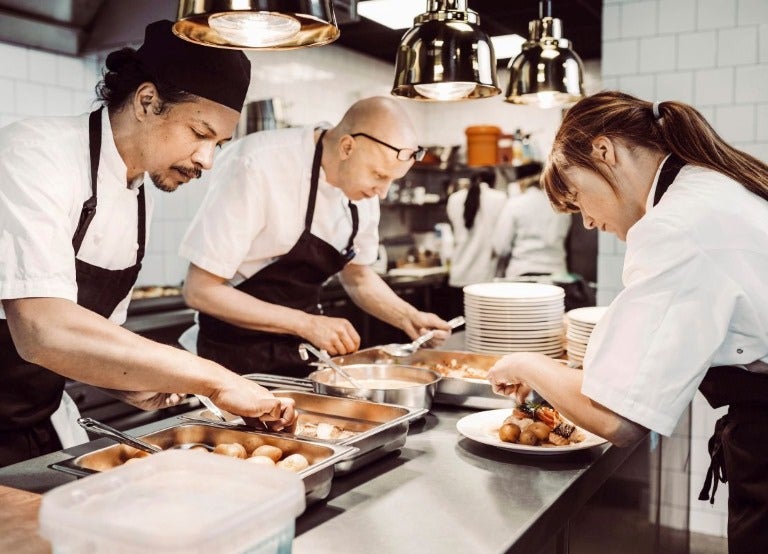 Equipo de cocina preparando platos simultáneamente en estación de trabajo con utensilios
