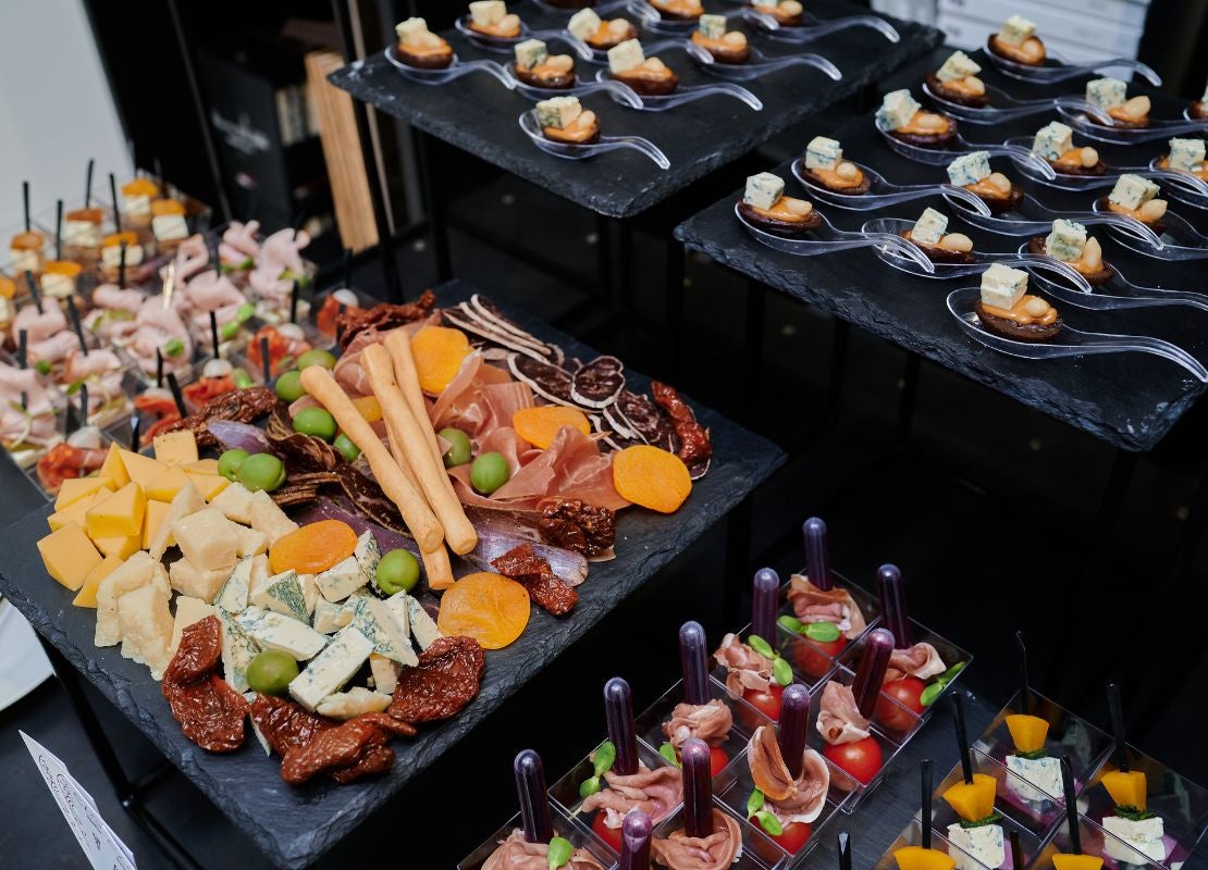 Tabla de quesos y embutidos junto a aperitivos individuales variados servidos en un catering.