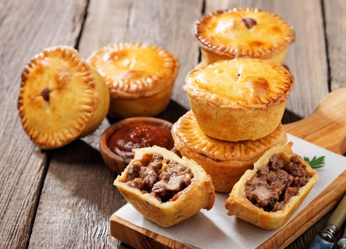 Pequeños pasteles salados de hojaldre rellenos de carne picada sobre tabla de madera rústica.