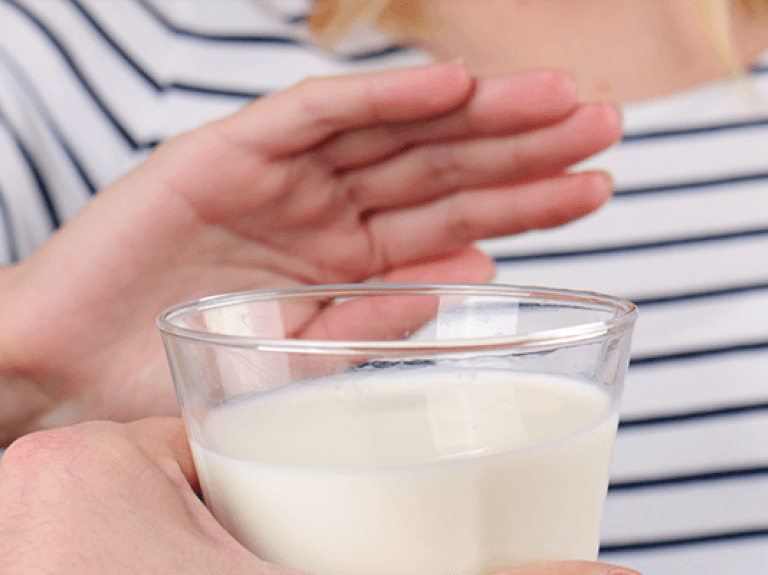 Mano de mujer rechaza vaso de leche porque es intolerante a la lactosa