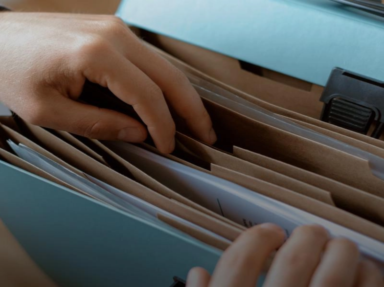 Manos buscando un documento dentro de una carpeta de archivo