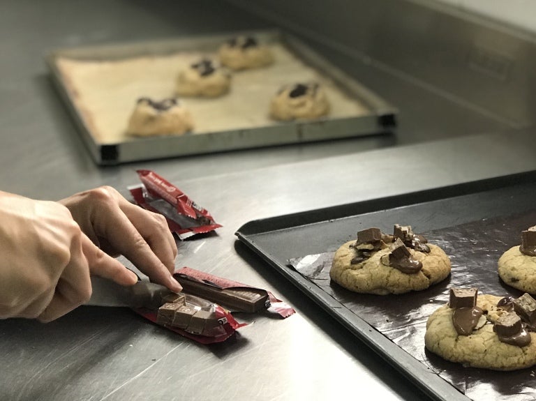 Manos cortando barras de chocolate kitkat para decorar galletas